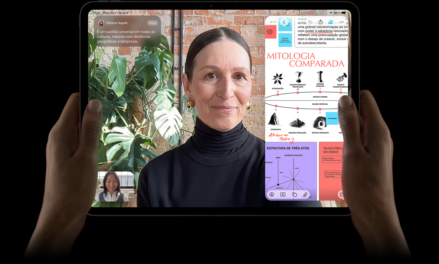 Parte da frente do iPad Pro preto-espacial, com as m?os esquerda e direita segurando o aparelho na horizontal, tela com borda preta mostrando uma conversa no FaceTime sendo traduzida ao vivo e um app educativo mostrando uma apresenta??o sobre Mitologia Comparada com textos, diagramas e anota??es manuscritas