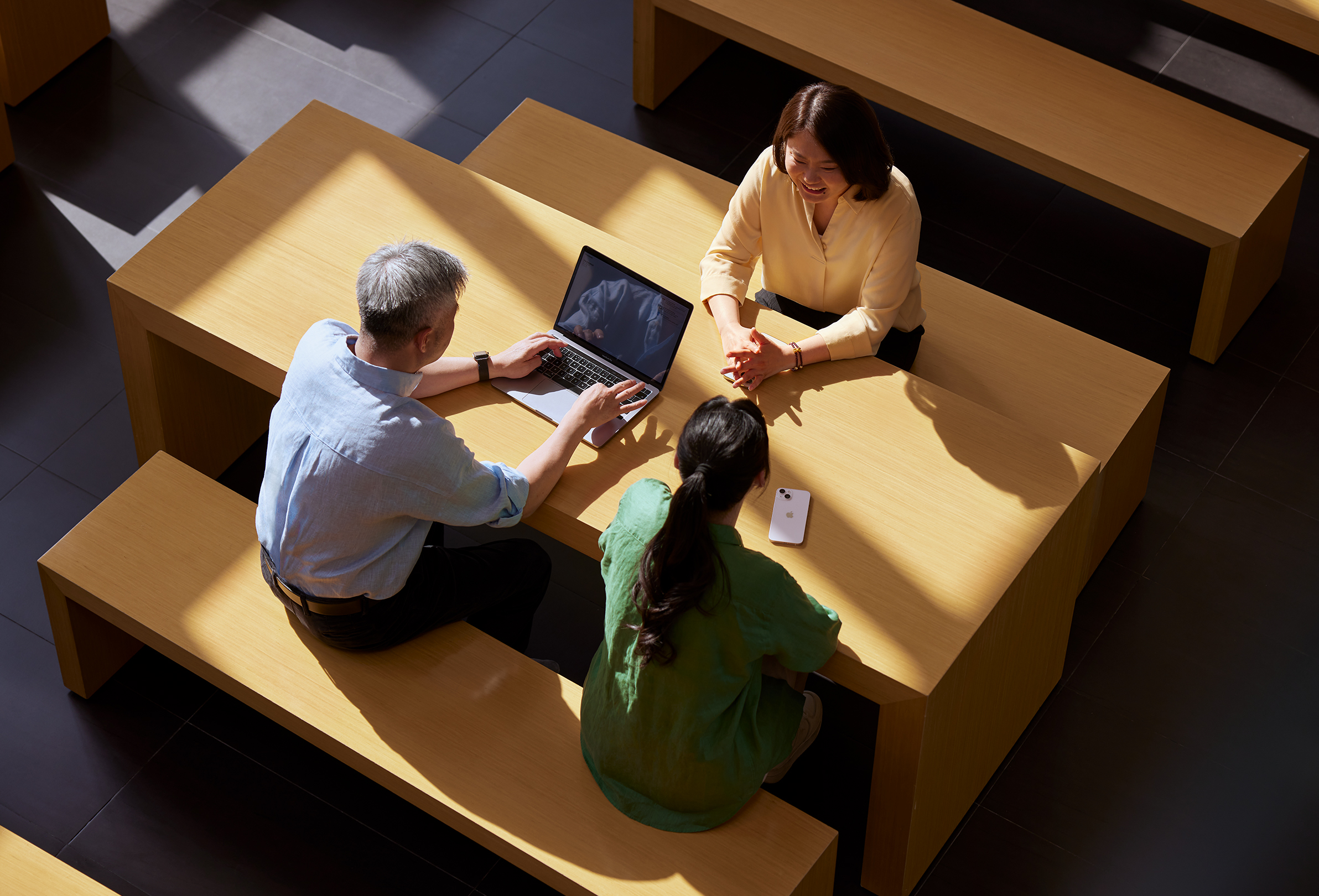 3人のApple社員が一緒に座り、1人はMacBookで作業(yè)している。