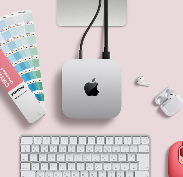 デスク上に置かれたシルバーのMac miniを上から見た図。AirPods、ピンクのワイヤレスキーボード、ピンクのワイヤレスマウス、短冊型の色見本が一緒に配置されている