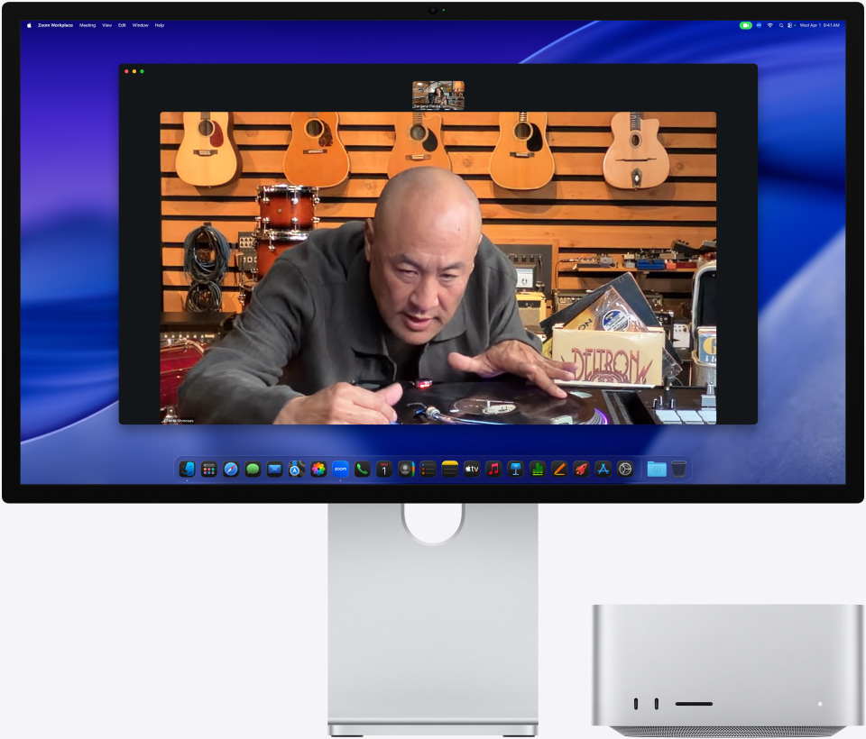 Asmuo, kalbantis vaizdo skambu?iu per ?Studio Display XDR“, po kuriuo pad?tas ?Mac Studio“, muzikos parduotuv?je, ?iūri ? patefon?